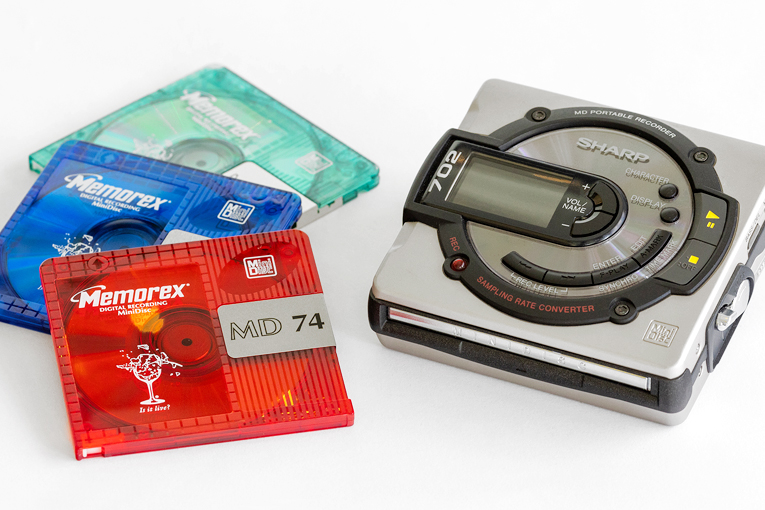 A pile of Memorex MiniDiscs next to a Sharp MD-MS702 player